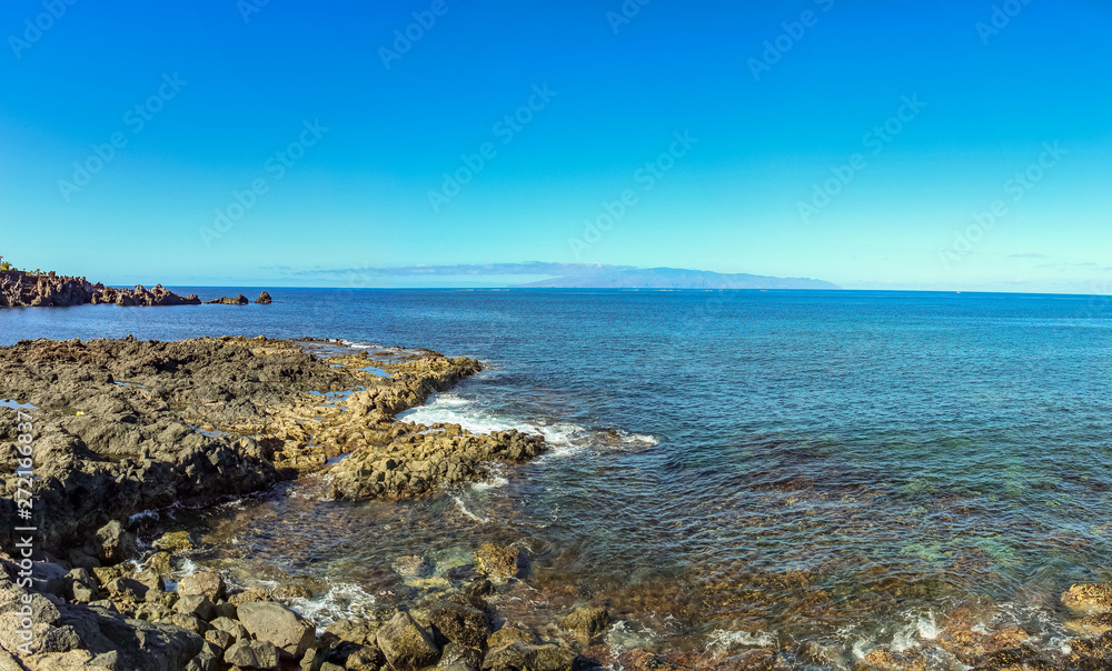 Steep high lava rock cliffs. Blue sea horizon, natural sky background.