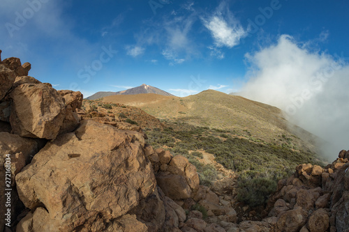 Mountains around volcano Teide, partly covered by the clouds. Bright blue sky. Teide National Park, Tenerife, Canary Islands, Spain.