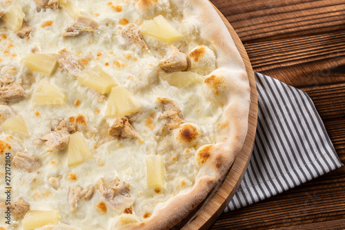 Pizza topped with sauce, chicken, cheese and pineapple serve on wooden plate on wooden table. Photo of Hawaiian pizza. 