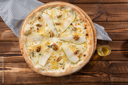 Traditional pizza with pear, nuts and blue cheese on a wooden background. Close up. Top view.