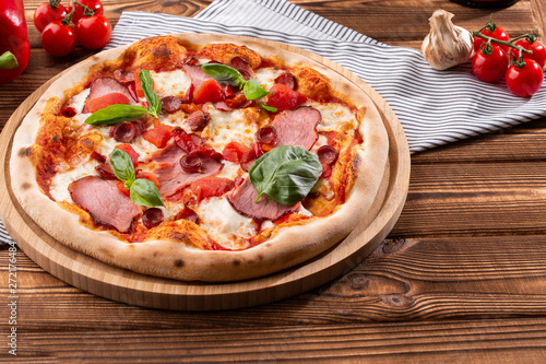 Pizza with ham , arugula (salad rocket), rucola and mozzarella on wooden background close up. Italian cuisine.
