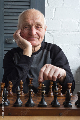 An old man is sitting in front of a chessboard, thinking and making the first move in the game photo