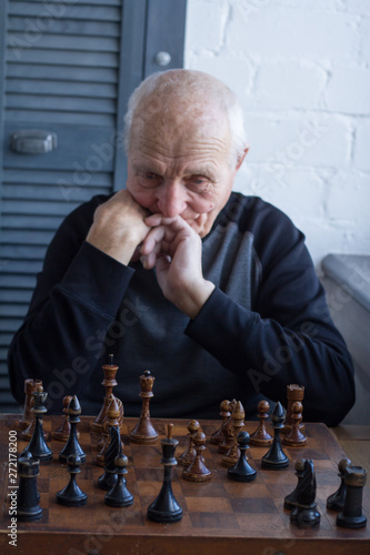 An old man is sitting in front of a chessboard, thinking about the next move in a chess game photo