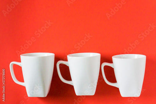 3 white winter coffee cup mugs lined up in a row for a break time meeting; Copyspace with empty room space for copy text on red horizontal background; Christmas holiday or Valentines.