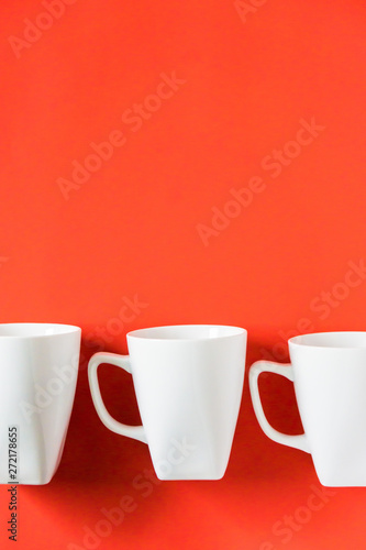 3 white winter coffee cup mugs lined up in a row for a break time meeting; Copyspace with empty room space for copy text on red vertical background; Christmas holiday or Valentines.
