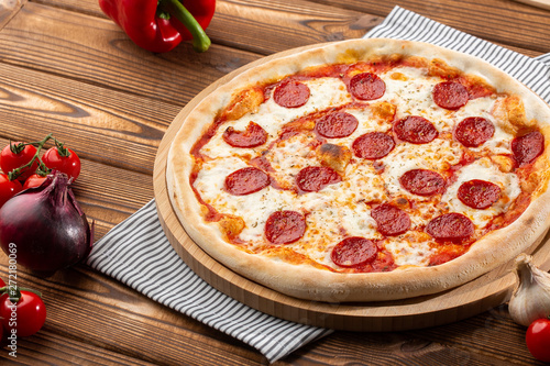 Delicious hot homemade Pepperoni pizza on the wooden table. Pepperoni Pizza - Fresh homemade pizza with pepperoni, cheese and tomato sauce on rustic black stone background wirh copy space.   photo