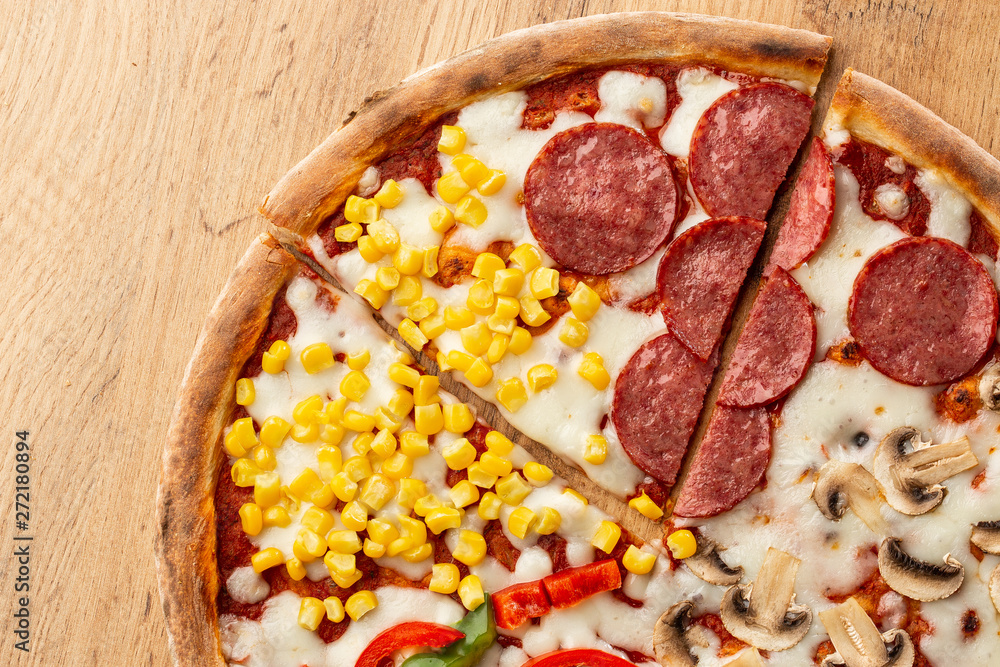 Delicious italian pizza with meat, vegetables cheese 4 seasons isolated on wooden background. Quattro Stagioni pizza with mozzarella, ham, bacon, mushrooms, salami, mozzarella, corn, sweet pepper . Delicious italian pizza with meat, vegetables cheese 4 seasons isolated on wooden background. Quattro Stagioni pizza with mozzarella, ham, bacon, mushrooms, salami, mozzarella, corn, sweet pepper .
