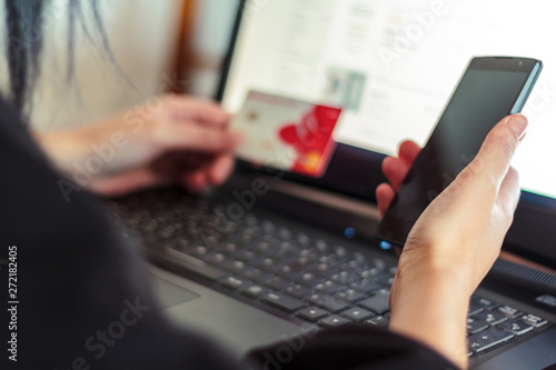 Woman using smartphone and laptop computer for online shopping at home with credit card