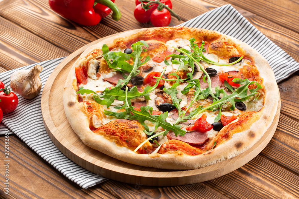 Pizza with ham , arugula (salad rocket), rucola, mushrooms olives and mozzarella on wooden background close up. Italian cuisine. Pizza with ham , arugula (salad rocket), rucola, mushrooms olives and mozzarella on wooden background close up. Italian cuisine.