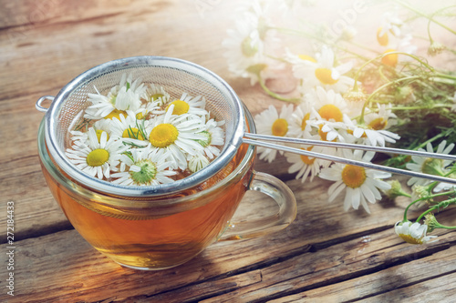 Daisy flowers in tea infuser and healthy chamomile herbal tea cup. photo