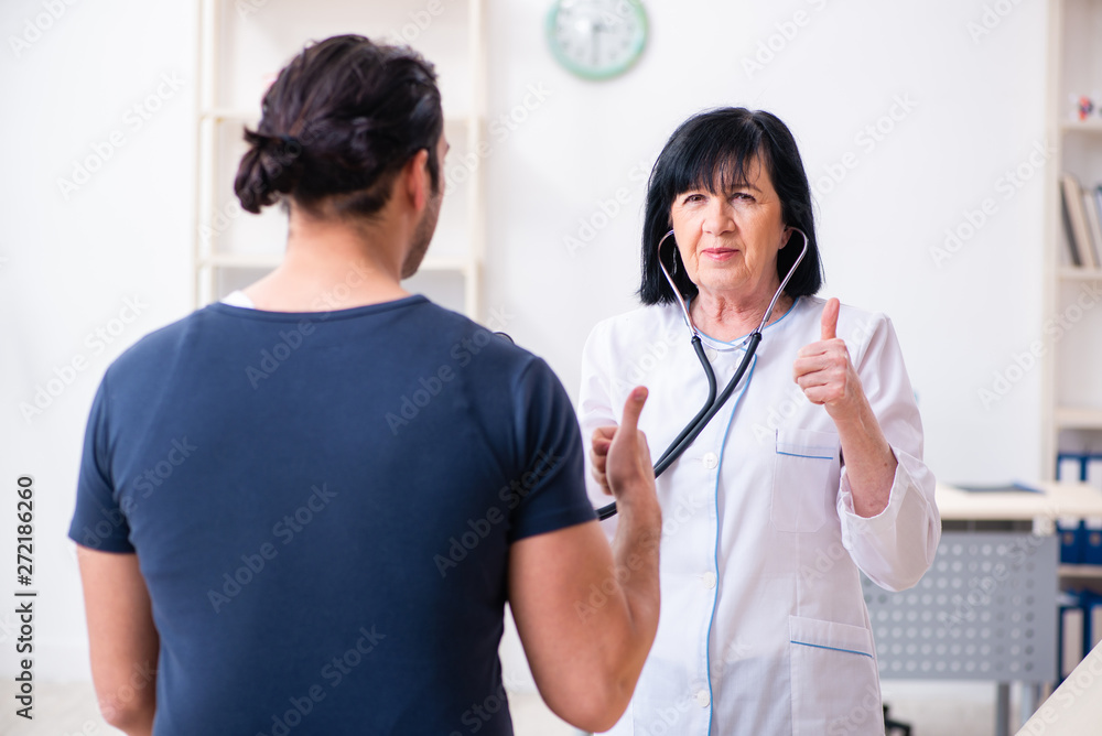 Young male patient visiting aged female doctor Young male patient visiting aged female doctor