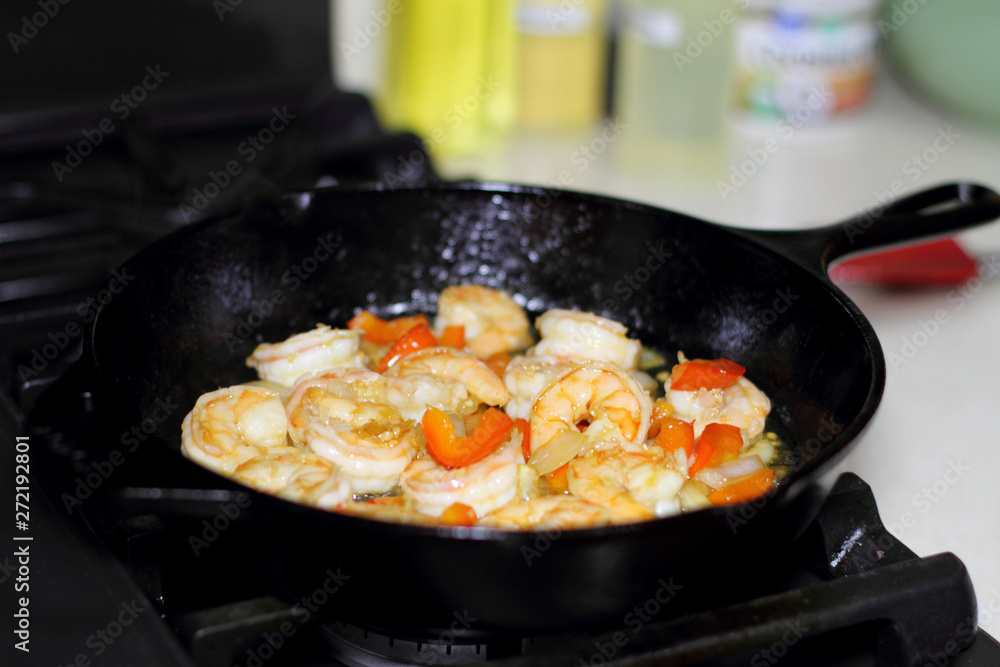 Shrimp cooking with red bell peppers and onion in a cast iron skillet on the stove. Shrimp cooking with red bell peppers and onion in a cast iron skillet on the stove.