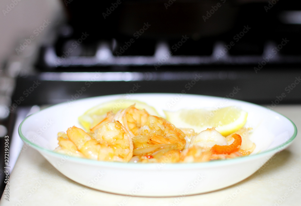 Plate of shrimp cooked with red bell peppers and onions, with slices of lemon.