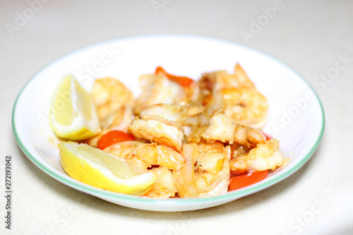 Plate of shrimp cooked with red bell peppers and onions, with slices of lemon.