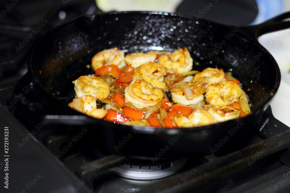 Shrimp cooking with red bell peppers and onion in a cast iron skillet on the stove. Shrimp cooking with red bell peppers and onion in a cast iron skillet on the stove.