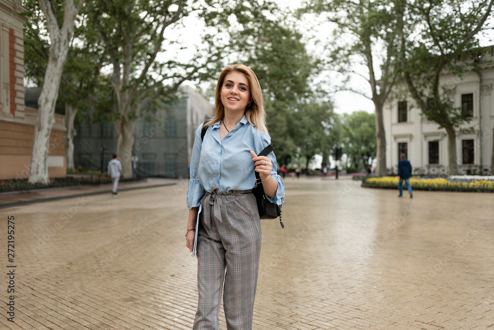 A pretty student walks around a university campus with a backpack and smiles.