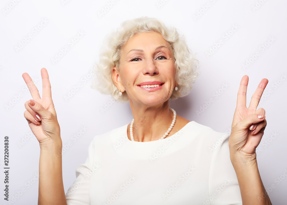 Old woman laugh and showing peace or victory sign at camera. Emotion and feelings. Portrait of expressive grandmother. Old woman laugh and showing peace or victory sign at camera. Emotion and feelings. Portrait of expressive grandmother.