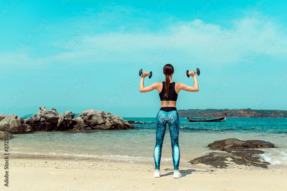 Girl with a perfect body training on a summer beach with a dumbbells. Sport, fitness, exercise and dieting concept. Girl with a perfect body training on a summer beach with a dumbbells. Sport, fitness, exercise and dieting concept.