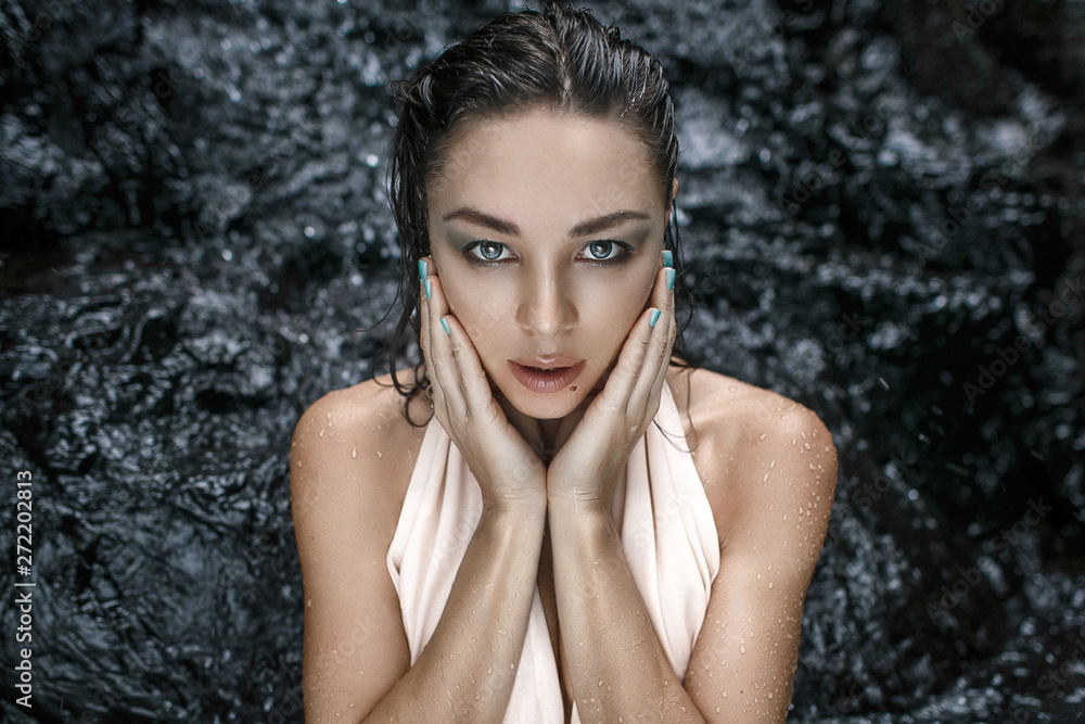 Fototapeta premium Close up portrait of a very beautiful woman in white dress posing for the camera. Blurred black cliff/rocks background