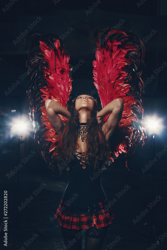 Delicate beautiful brunette woman posing with  red dark angel wings. Studio shot.