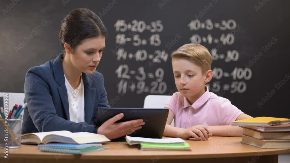 Young teacher showing schoolboy information on tab, private lesson, innovations Young teacher showing schoolboy information on tab, private lesson, innovations