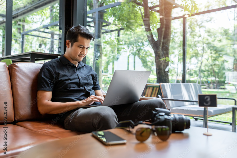Asian man using gadgets Inspired, Confident young man working on laptop while sitting at his working place in coffee shop, Freelance work concept. Asian man using gadgets Inspired, Confident young man working on laptop while sitting at his working place in coffee shop, Freelance work concept.