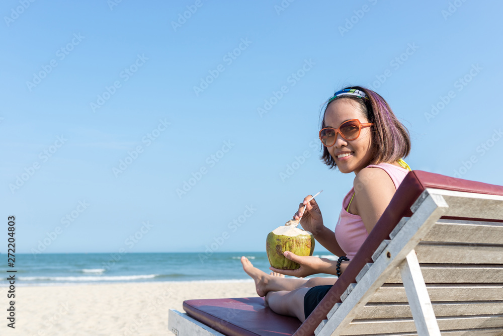 Asian woman enjoy drinking fresh coconut on summer beach chair