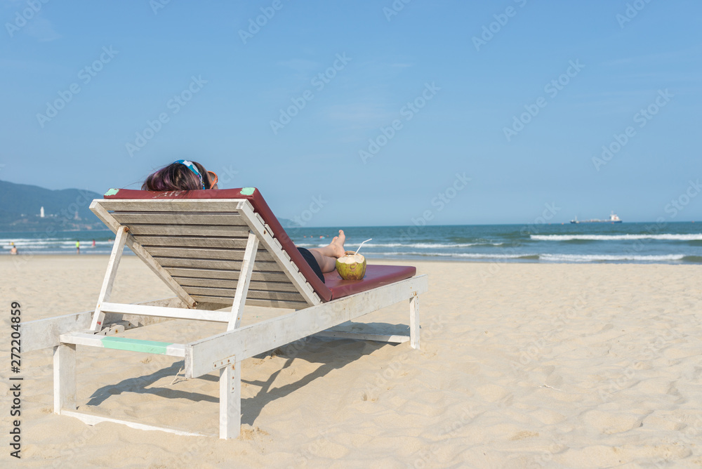 Obraz premium Rear view of woman lying on sandy summer beach chair 