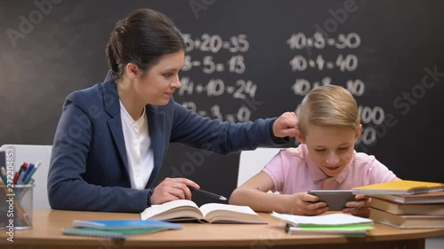 Irritated lady teacher grabbing boys playing on smartphone ear, punishment photo