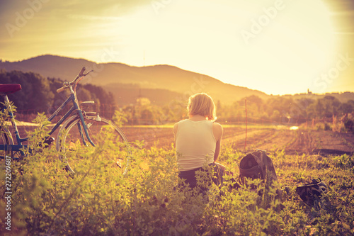 Fotografie Enjoying the evening sun, sundown scenery: woman with bike is sitting in the gre
