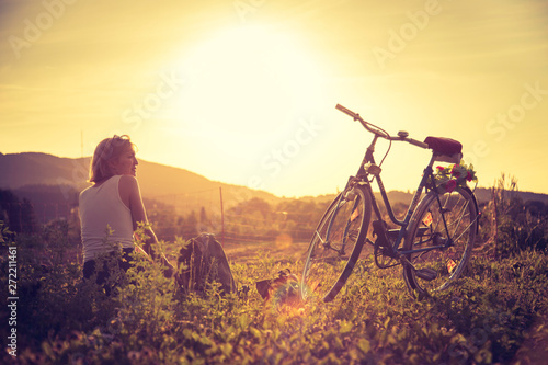 Enjoying the evening sun  sundown scenery  woman with bike is sitting in the green grass