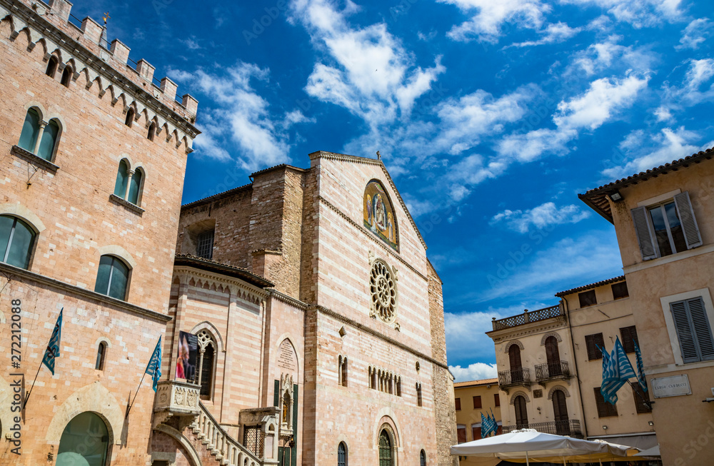 The Cathedral of San Feliciano in the square of Foligno. The main facade, with the rose window, mullioned windows, arches and columns. The blue flags of the neighborhood. The blue sky. Umbria, Italy.