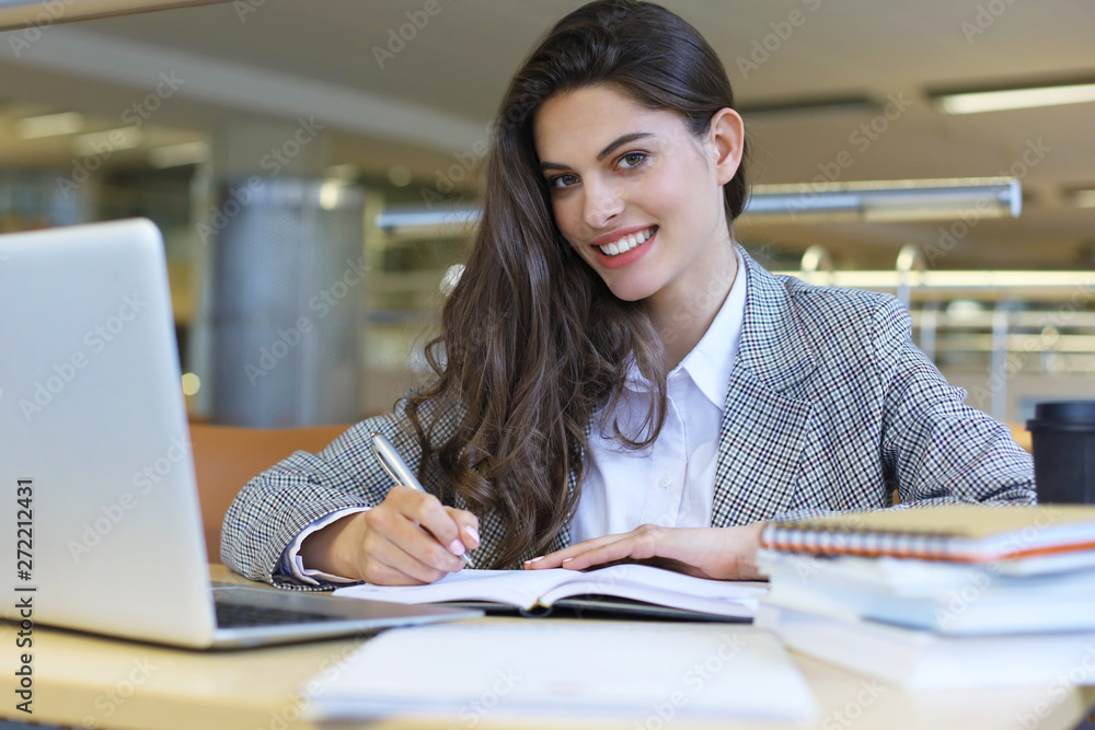 Portrait of a pretty female student with laptop in library. Portrait of a pretty female student with laptop in library.