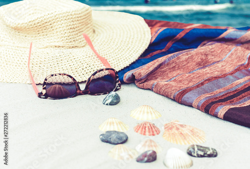 Straw hat, cover-up beachwear wrap and sun glasses on a tropical beach.
