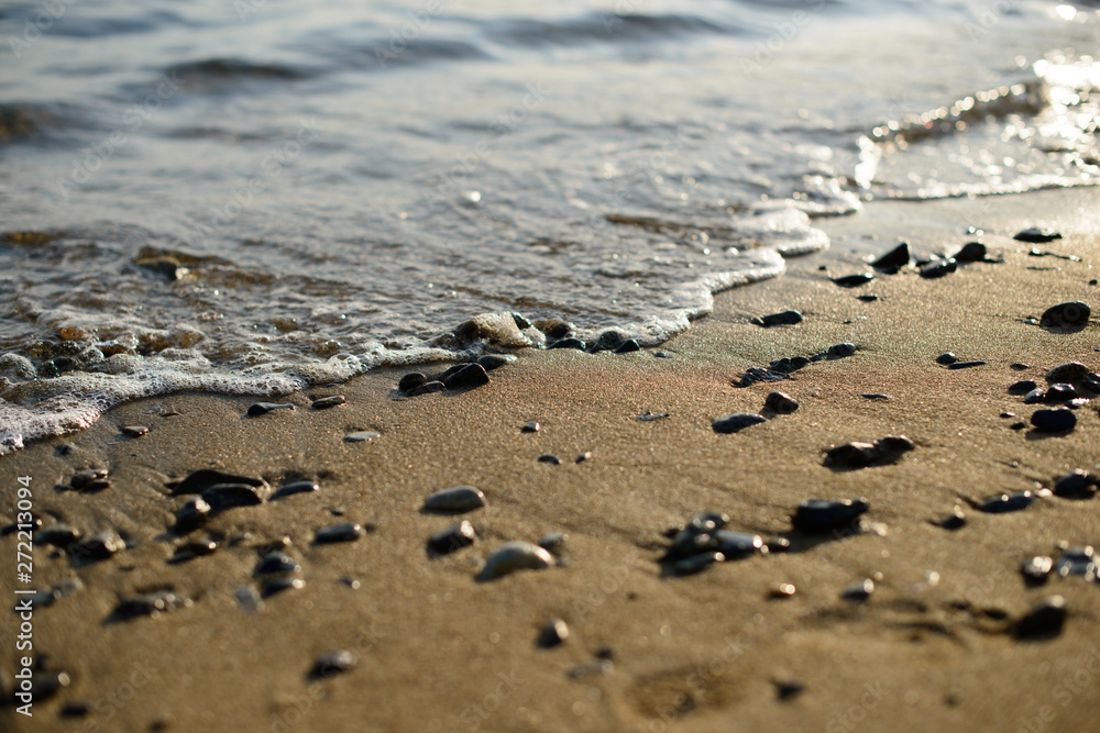 Wet pebbles on seashore in evening sun light. Sea wave on seacoast with round stones. Wet pebbles on seashore in evening sun light. Sea wave on seacoast with round stones.