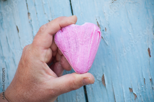 closeup of pink stone pebble in shaped heart in hand on blue wooden shutter in outdoor - Love concept