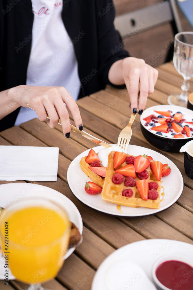 Sweet breakfast in the summer cafe. On a wooden table, a dessert waffles with a scoop of ice cream and fruit berries of strawberry and raspberry. Golden cutlery in the hands.