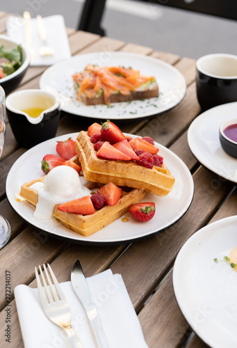 Sweet breakfast in the summer cafe. On a wooden table, a dessert waffles with a scoop of ice cream and fruit berries of strawberry and raspberry.