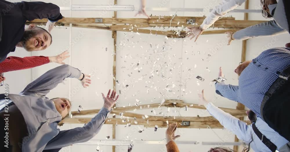 Close-up happy multiethnic group of business people joining hands together, clapping under confetti at office background
