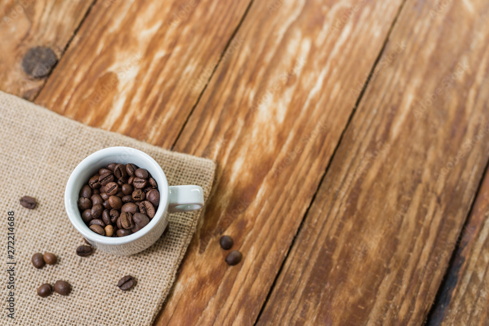 Delicious brown coffee beans in an Italian espresso cup on a wood table.. Delicious brown coffee beans in an Italian espresso cup on a wood table..