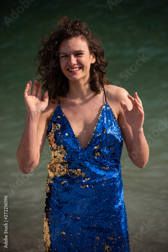 Portrait of a chestnut girl with wavy brown hair in a mountain lake. Wear a dress with light blue straps with gold applications. Beautiful light, he keeps his hands open as if by surprise.