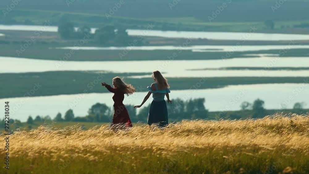 Two women dancing and laughing in summer field on the background of the lake. Two women dancing and laughing in summer field on the background of the lake.