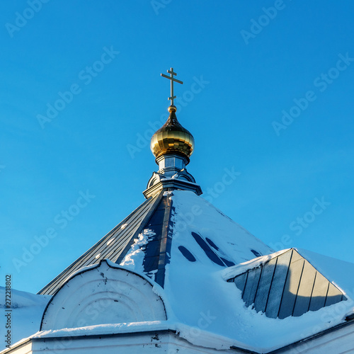 Before us is the snow-covered roof of one of the buildings of the Perm Holy Trinity Stefanov monastery. Against the blue sky stands a gilded tower. photo