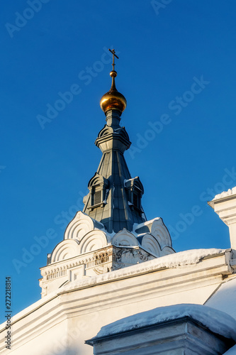 The roof and gilded dome of the bell tower are visible behind the wall of the Perm Holy Trinity Stefanov monastery. Winter. It is sunny. photo