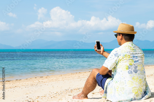 Young asian man on the beach using smartphone.