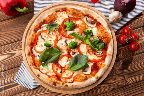 Vegetarian pizza on a wooden background with mushrooms, broccoli, cheese and sweet pepper and basil. Top view.