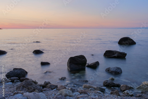 sunset in the sea with black rocks in the front. long shutter time. blurry sea with red sky