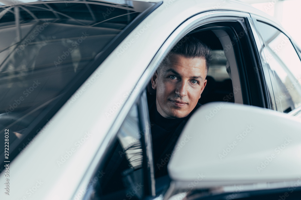 Handsome elegant serious man drives a white modern car Handsome elegant serious man drives a white modern car
