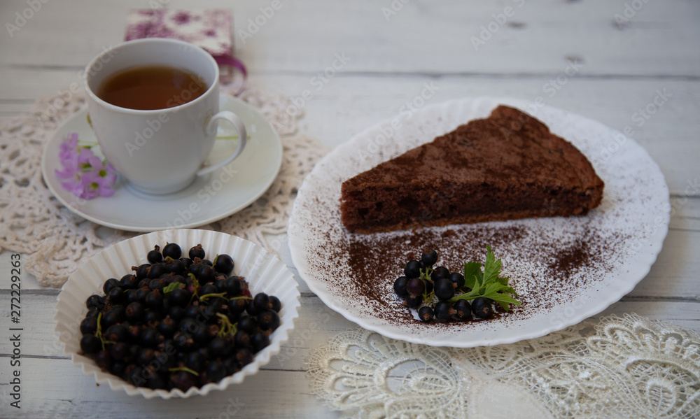 chocolate cake slice with a white cup of tea and a handful of currants chocolate cake slice with a white cup of tea and a handful of currants