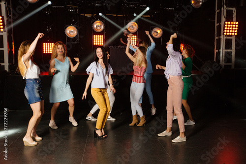 Eight female smart dancers having big fun moving at disco night club while raising their arms during holidays party relaxing celebrating dancing at party in night club together. Full height portrait